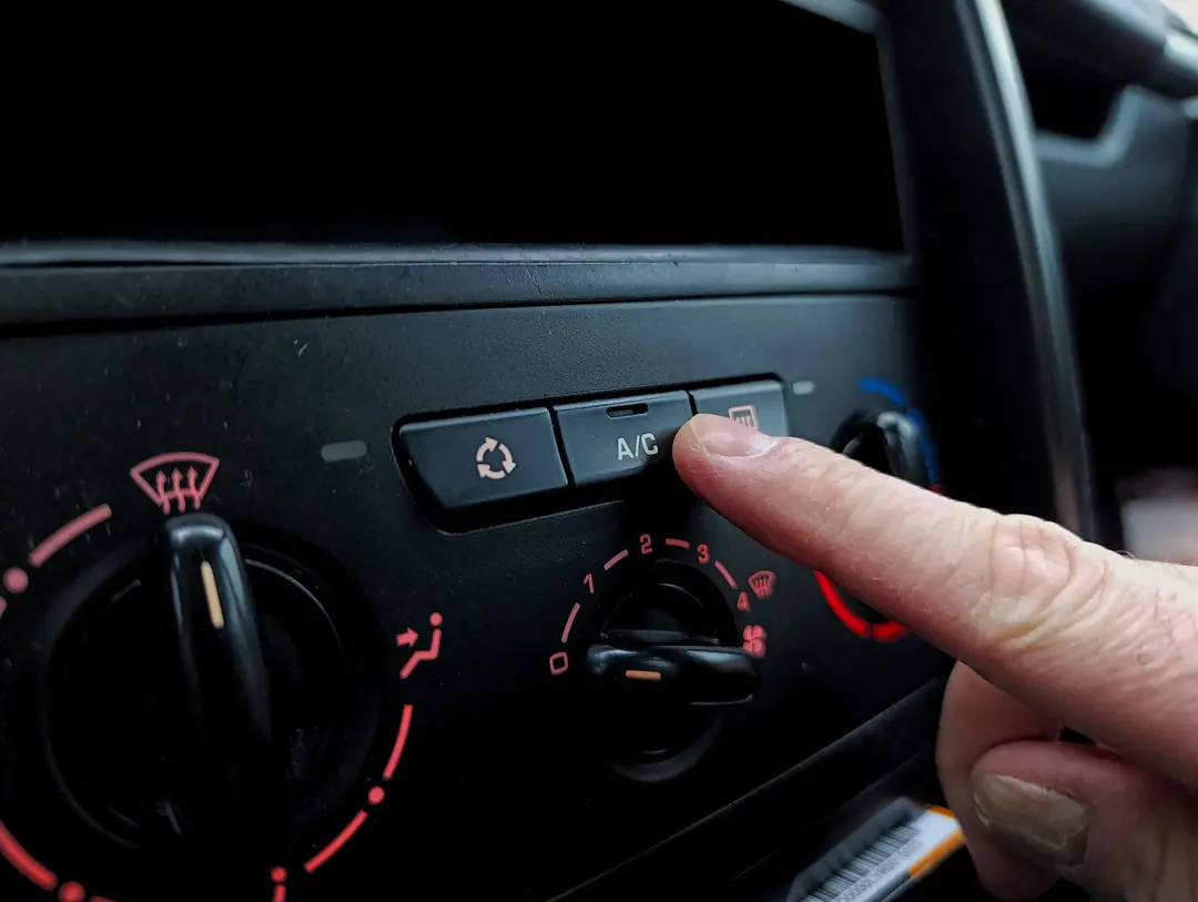 Mão acionando o botão A/C no painel de controle do ar condicionado automotivo