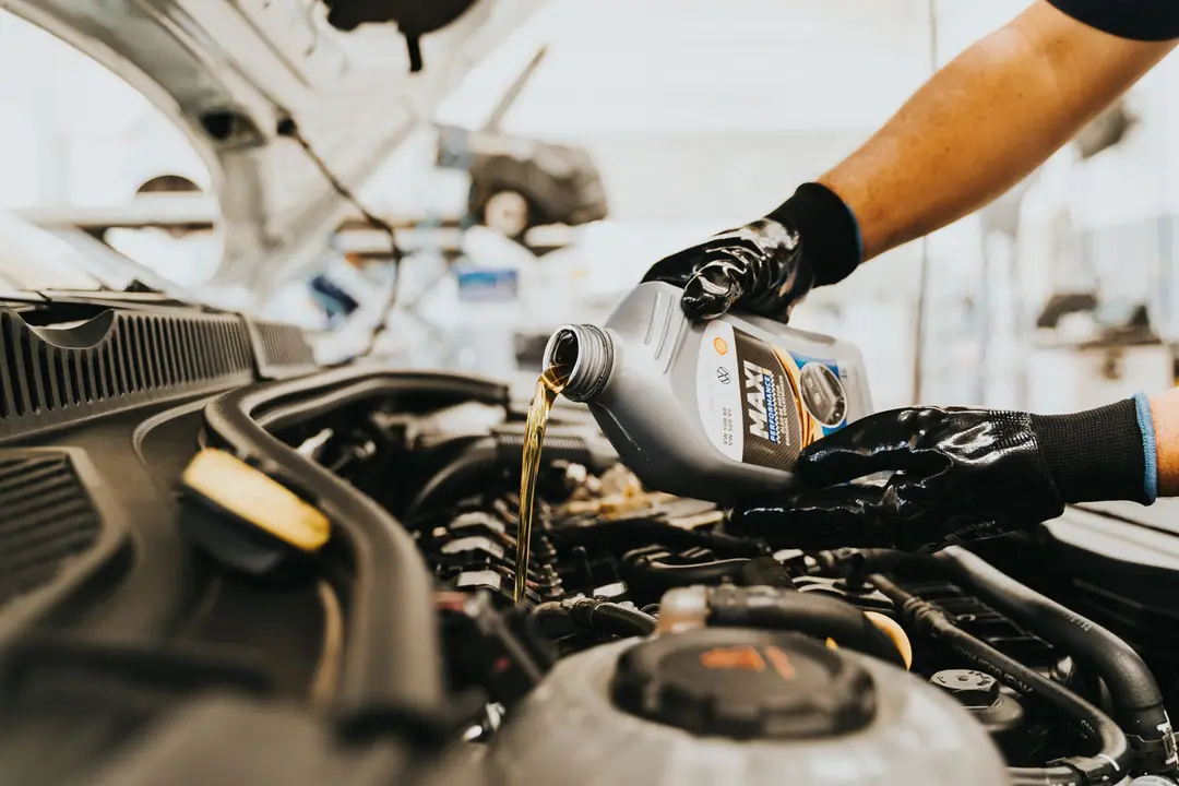 Mecânico despejando óleo lubrificante novo no motor de um carro durante troca de óleo em oficina