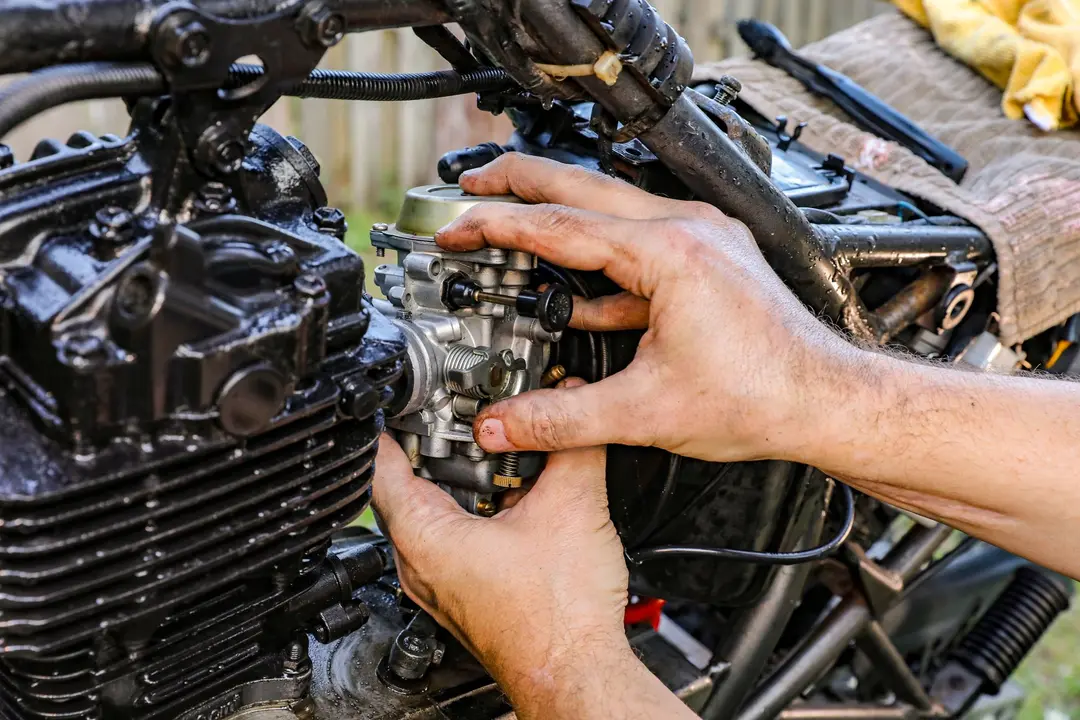 Mãos de mecânico ajustando carburador de motor de motocicleta, trabalhando em peças metálicas do sistema de alimentação